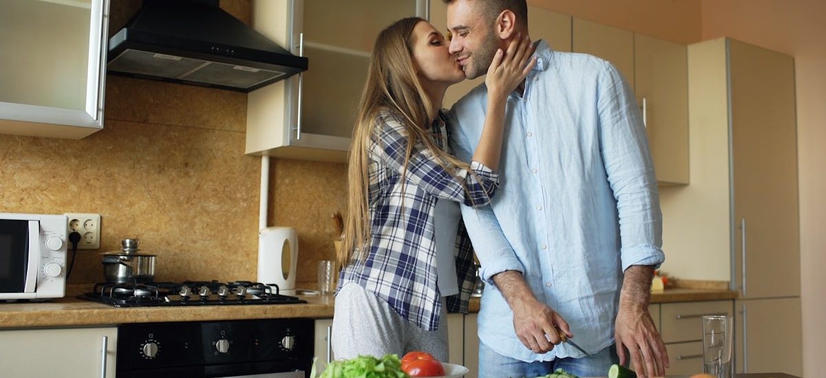 Happy young couple embracing and talking in the kitchen while cooking breakfast at home in the morning