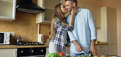 Happy young couple embracing and talking in the kitchen while cooking breakfast at home in the morning