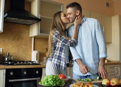 Happy young couple embracing and talking in the kitchen while cooking breakfast at home in the morning