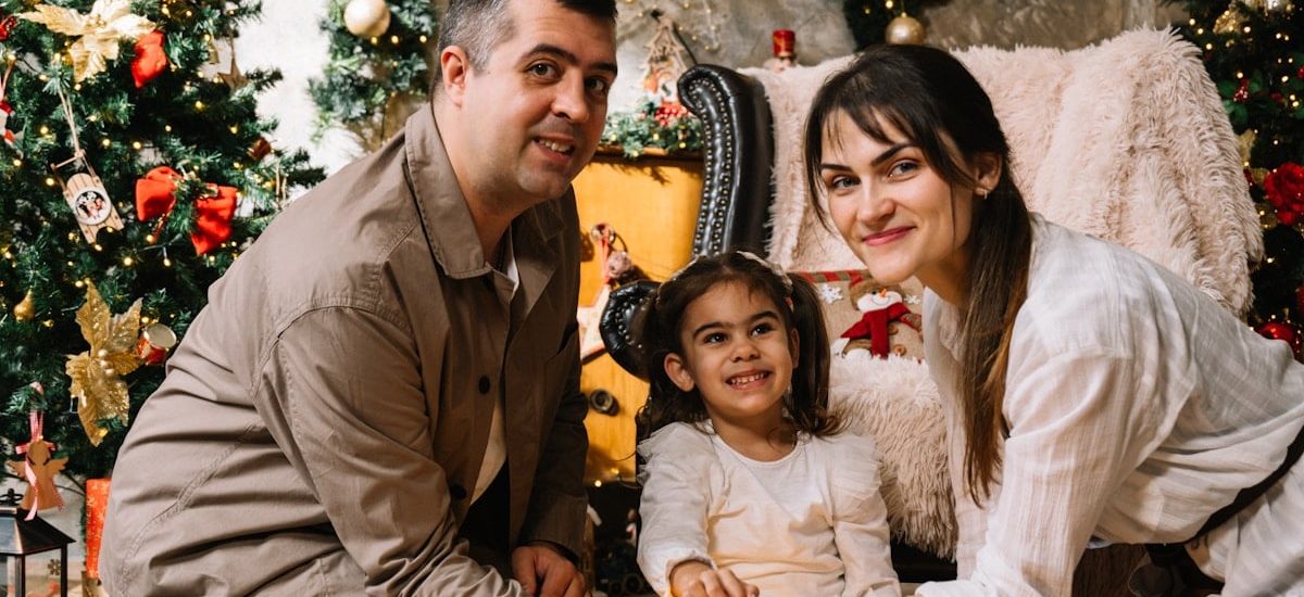 A man and a woman sitting next to a little girl in front of a christmas
