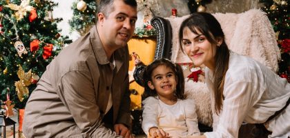 A man and a woman sitting next to a little girl in front of a christmas