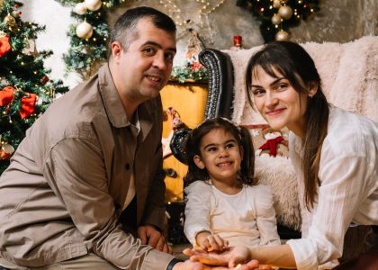 A man and a woman sitting next to a little girl in front of a christmas